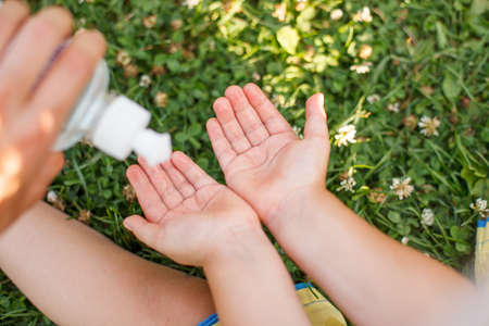 Life during coronavirus pandemic. Mother and daughter disinfecting hands with sanitizer outdoors in city park, summer hygiene healthcare concept, lifestyle, selective focus, antibacterial antisepticの写真素材