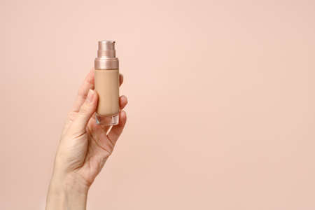 Hand holding makeup liquid found, Applying foundation for makeup. Woman's hands with neutral...