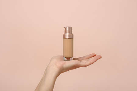 Hand holding makeup liquid found, Applying foundation for makeup. Woman's hands with neutral manicure holding bottle of concealer or toner foundation, copy space, banner, flyerの写真素材