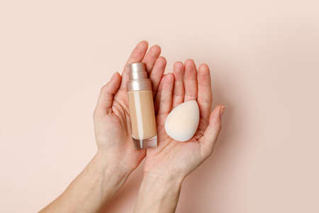 Female Hands holding makeup liquid found or concealer and make up beuty blender or egg sponge on...