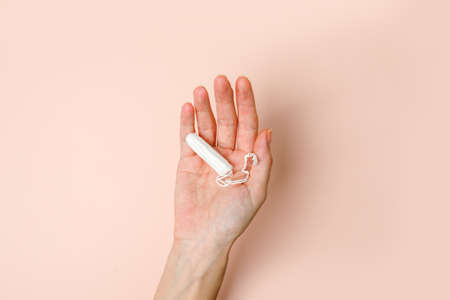 Woman hand holding Medical female tampons on beige background. Hygienic white organic tampon for women. Cotton swab. Menstruation, means of protection. Stylish minimal concept, bannerの写真素材