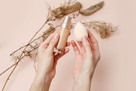 Foundation with make up beuty blender in female hands on a trendy beige brown earth tones...
