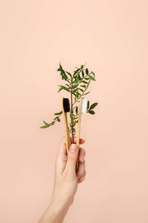 Eco-friendly bamboo tooth brush in woman hand. Zero waste set on light beige natural background, copy space. Daily healthcare, oral care routine, trendy tools for bathroomの写真素材