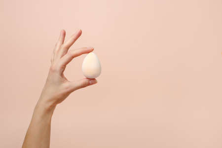 Cosmetic sponge beauty blender in woman hand on a beige background, modern trendy still life, monochrome, earth tones, neutral shades, beauty industry, makeup artist, face care, copy spaceの写真素材