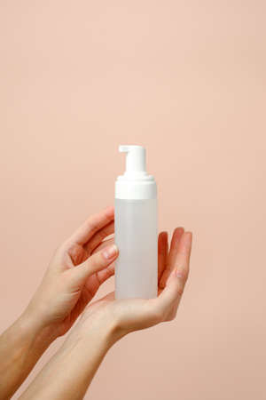 Female hand with cosmetic product in bottle on neutral beige trendy background, concept of helathcare, hygiene, dispenser with soap or antiseptic antimicrobial gel, minimalismの写真素材