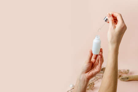 Woman hands holding facial essential oil or serum packaging on beige trendy neautral earth tones...