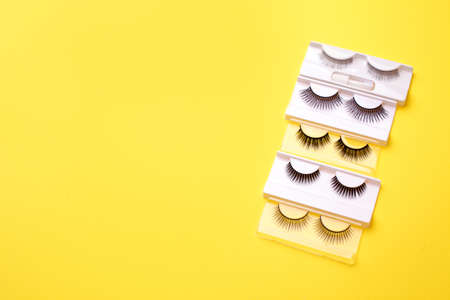 Flat lay composition of professional makeup tools and false eyelashes on bright yellow background,...
