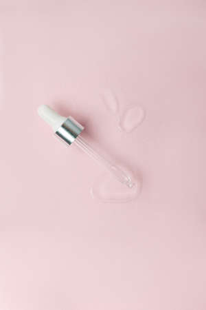 Cosmetic pipette with a drop close up on pink pastel background, vertical. Beautician, cosmetology minimal stylish concept, wellness, skincare, face tune, moisturizing treatmentの写真素材