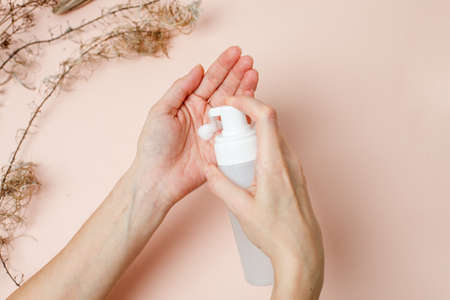 Woman pressing the liquid soap to her hand on trendy beige neautral earth tones background, hygiene, skincare, wellness concept. Antibacterial antiseptic product during coronavirus pandemic.の写真素材