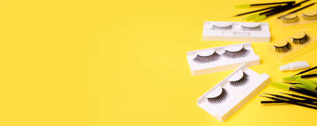 Different tools for eye lash extension on trendy bright yellow background. Fake eyelashes, brushes and clay. Beauty concept, makeup cosmetics. Place for text and design. Banner, flyerの写真素材