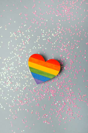 Painted paper heart like a LGBT pride rainbow flag on gray background with star confetti. LGBT...