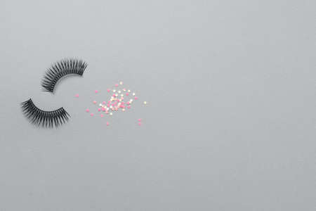 Fake eyelashes and sparkling confetti on trendy gray color background. Beauty concept. Makeup cosmetics. Top view, flat lay. Layout. Place for text and design. Web Banner. Minimal styleの写真素材