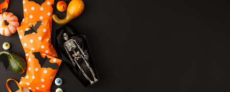 Happy Halloween holiday concept. Decorative skeleton of man in paper handmade coffin and traditional candy bags on black background. Halloween party greeting card, invitation, banner, flyerの写真素材