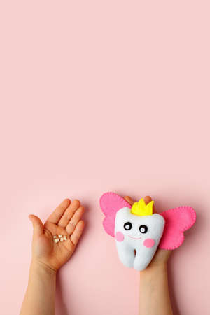 Little child holding felt tooth fairy toy in his hands on pink background. Easy and funny kids crafts, DIY, Happy Tooth Fairy greeting card, flyer, copy space, concept of tooth changesの写真素材
