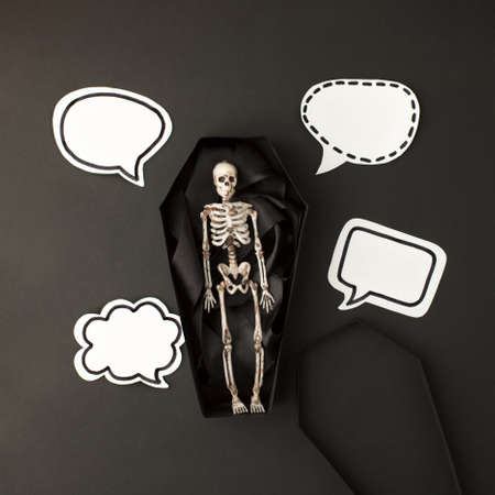 Halloween party concept - toy skeleton in coffin speaking bubbles for text on black background, creative invitation for night party, promotion flyer, banner for site, message, chatingの写真素材