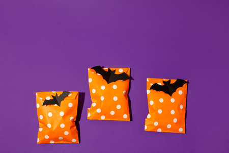 Halloween holiday concept with party gift paper bag decor and candy corn on bright violet purple...