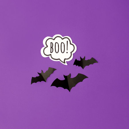Halloween bats decorations and chat bubble boo on purple background. Flat lay, top view, minimal style, copy space.の写真素材