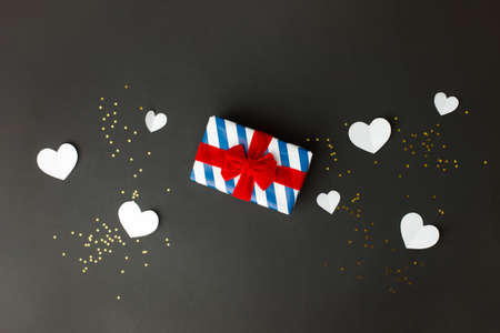 Stylish gift box with blue stripes and red bow, paper hearts on black background, copy space, Greeting card, banner, flyer, postcard for Saint Valentine day, Black friday sale, Xmas, New year birthdayの写真素材