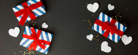Stylish gift box with blue stripes and red bow, paper hearts on black background, copy space, Greeting card, banner, flyer, postcard for Saint Valentine day, Black friday sale, Xmas, New year birthdayの写真素材