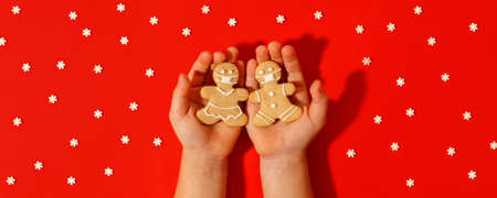 Happy 2022 New Year's set of cookies, gingerbread man, woman in face from ginger biscuits glazed sugar decoration in kids hands on red background, minimal seasonal pandemic winter holidayの写真素材