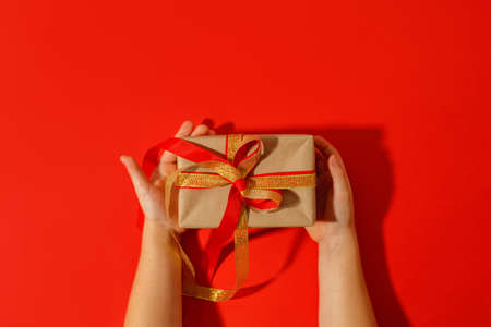 Kids hands holding decorativegift box with bow on red background. Sale, Holiday, greering card Happy new year 2022, Merry Christmas, banner for your site, invitation, flyer, holiday invitationの写真素材