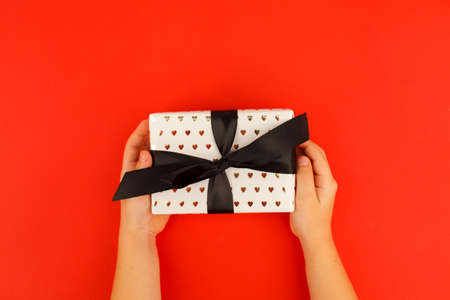 Kids hands holding decorativegift box with bow on red background. Sale, Holiday, greering card Happy...