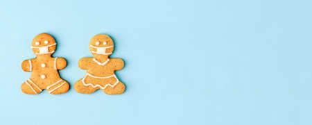Happy New Year's set of couple of gingerbread woman man in face mask from ginger biscuits glazed sugar icing decoration on blue background, minimal seasonal pandemic winter holiday banner, stay homeの写真素材