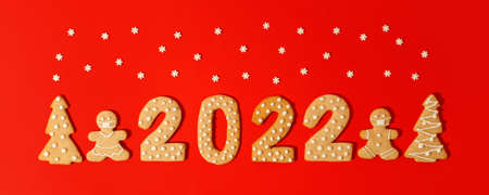 Happy New Year's set of numbers 2022, gingerbread Tree and gift from ginger biscuits glazed sugar icing decoration on red background, minimal seasonal pandemic winter holiday banner, stay homeの写真素材