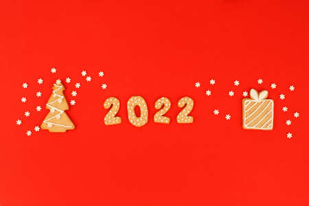 Happy New Year's set of numbers 2022, gingerbread Tree and gift from ginger biscuits glazed sugar icing decoration on red background, minimal seasonal pandemic winter holiday banner, stay homeの写真素材