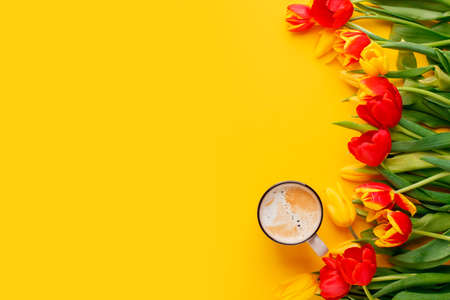 Beautiful spring breakfast on Mothers or Womans International day 8 march, Easter. Bouquet of red yellow tulips and coffee cup on bright yellow table top view. Flat lay, banner for site, seasonal flyerの写真素材