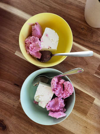 Vanilla and fruit berry ice cream in plastic plates, dessert spoons on woodan table. Homemade ice...