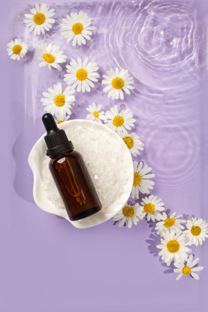 Dark glass cosmetic bottles with water drops on pastel purple violet background with chamomile flowers. Concept of natural moisturizing cosmetics for skin care, organic bio skincare flyerの写真素材