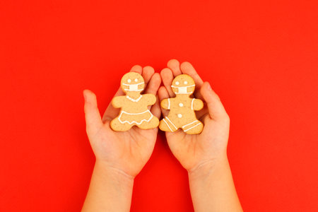 Happy 2023 New Year's set of cookies, gingerbread man, woman in medical face mask from ginger biscuits glazed sugar decoration in kids hands on red background, seasonal pandemic winter holidayの写真素材