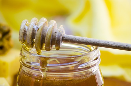 liquid honey in a glass jar with honey dipper for herの写真素材