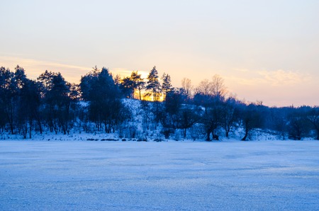 winter forest and a river covered in snow at sunsetの写真素材