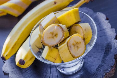 sliced bananas in a bowl on a dark wooden tableの写真素材
