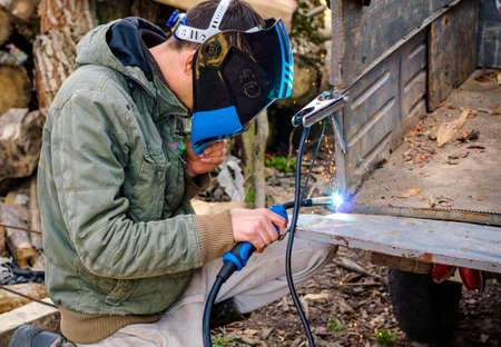 welder performs work at home with a semi-automatic welding machine in a protective mask without...