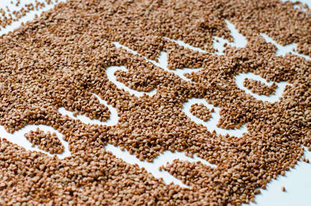 Raw fried buckwheat groats on a white plate with the name of the groatsの写真素材