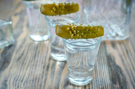 Vodka in a glass and pickled cucumber. Traditional Russian alcoholic drink with a snack