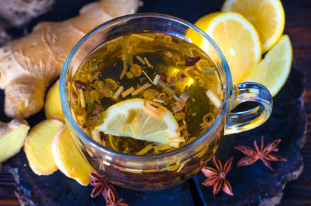 Healing herbal tea in a cup with lemon, honey and ginger on a dark backgroundの写真素材