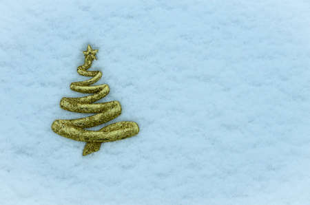 A figurine of a Christmas tree in golden color against a background of white-blue snowの写真素材