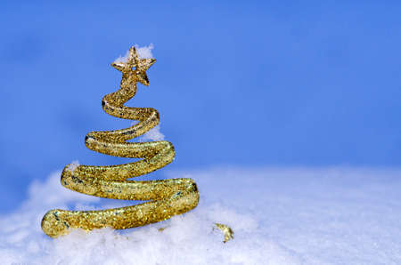 A figurine of a Christmas tree in golden color against a background of white-blue snowの写真素材