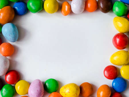 Small, chocolate, multi-colored candies in the form of a frame on a white background with space for writing text in the middleの写真素材