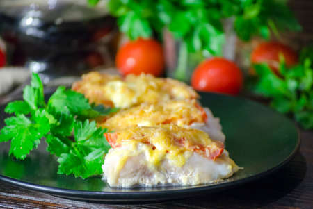 fish baked with vegetables and cheese in a white sauce on a dark backgroundの写真素材