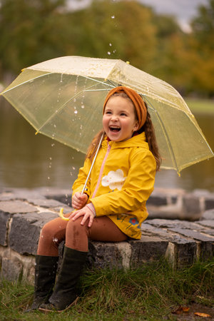 Happy little girl have a fun under umbrella in rain dayの写真素材
