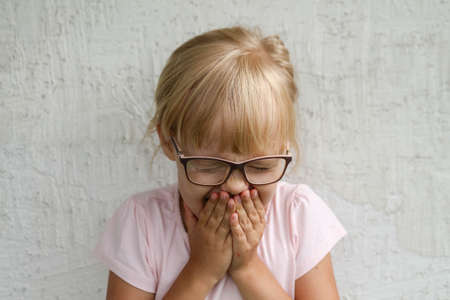 The child sneezes, covers his nose and mouth with his hands. Grey backgroundの写真素材