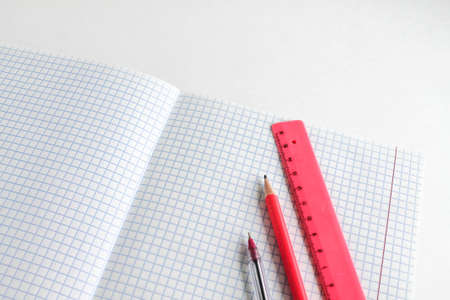 Stationery on a white background. A pen, pencil and ruler lie on a clean open sheet of a notebook
