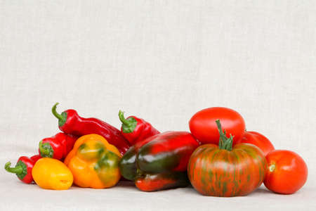 Bright colorful tomatoes and peppers of different sizes. Red, yellow, variegated, large and mini tomatoes on a beige background.の写真素材