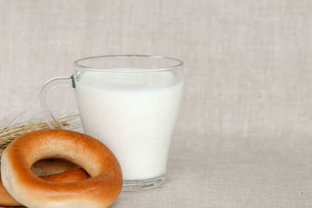 bagels, wheat ears and a glass of milk on a linen backgroundの写真素材