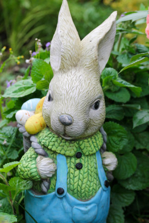 garden figure Easter bunny in blue jumpsuit with a backpack of colored eggs behind the back.の写真素材